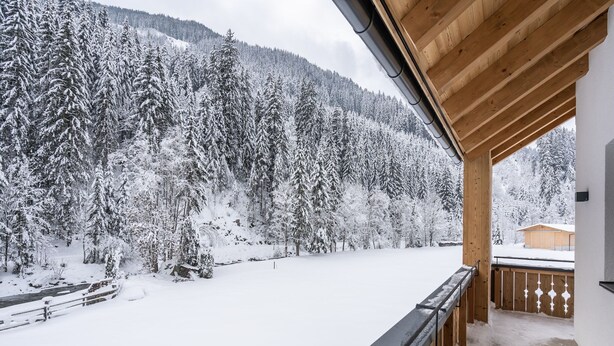 Un balcón de madera con vistas a un bosque nevado y montañas.