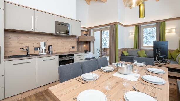 A modern kitchen with a dining area, wooden ceiling beams, and a large window with a view of snow-covered trees. - Chalet in Saalbach near Ski Lift (Saalbach-Hinterglemm)