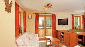 Un salón acogedor con un sofá, una mesa de madera, una televisión y vistas a un bosque a través del ventanal.