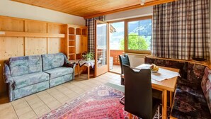 A cozy room with a wooden ceiling, a sofa, a dining table with chairs, and a view of greenery outside.
