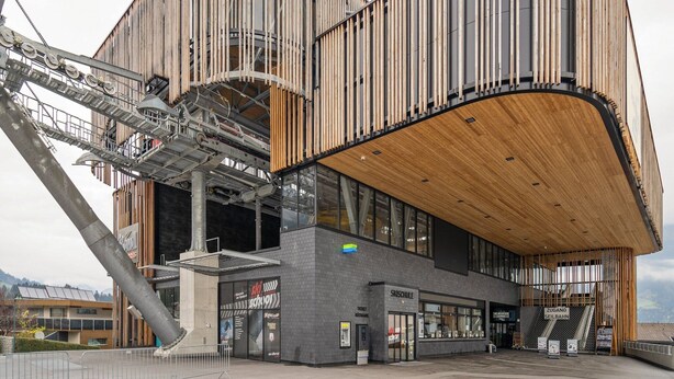 A modern building with a curved wooden facade, a ski school entrance, and a ski lift visible.