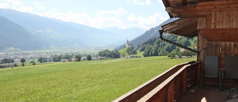 A wooden balcony with a view of a green field and distant mountains.