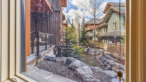 A view from a window overlooking a courtyard with a stone pathway, a small tree, and buildings with wooden facades. - Spacious Resort Condo | Near Banff (Canmore)