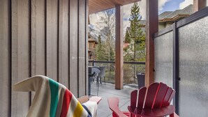 A covered outdoor area with a view of a mountain landscape, a table with chairs, and a colorful towel on a chair. - Spacious Resort Condo | Near Banff (Canmore)