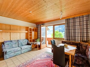 A cozy room with a wooden ceiling, a sofa, a dining table with chairs, and a view of greenery outside. - Apartment in Fügenberg near Ski Lift (Fügenberg)