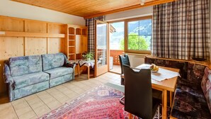 A cozy room with a wooden ceiling, a sofa, a dining table with chairs, and a view of greenery outside. - Apartment in Fügenberg near Ski Lift (Fügenberg)