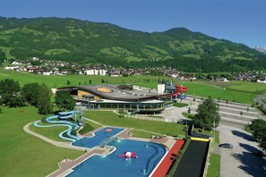 Ein modernes Gebäude mit Schwimmbad, Wasserrutschen und Blick auf eine bergige Stadt.