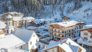 A snow-covered town with traditional wooden buildings, including a church with a spire, and a hotel with balconies. - Apartment in Gerlos near Ski Lift (Gerlos)