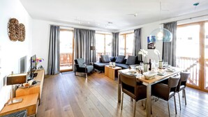 A modern living room with a wooden floor, a dining area with a table set for two, a sofa, and a TV on a wooden stand. - Apartment in Gerlos near Ski Lift (Gerlos)