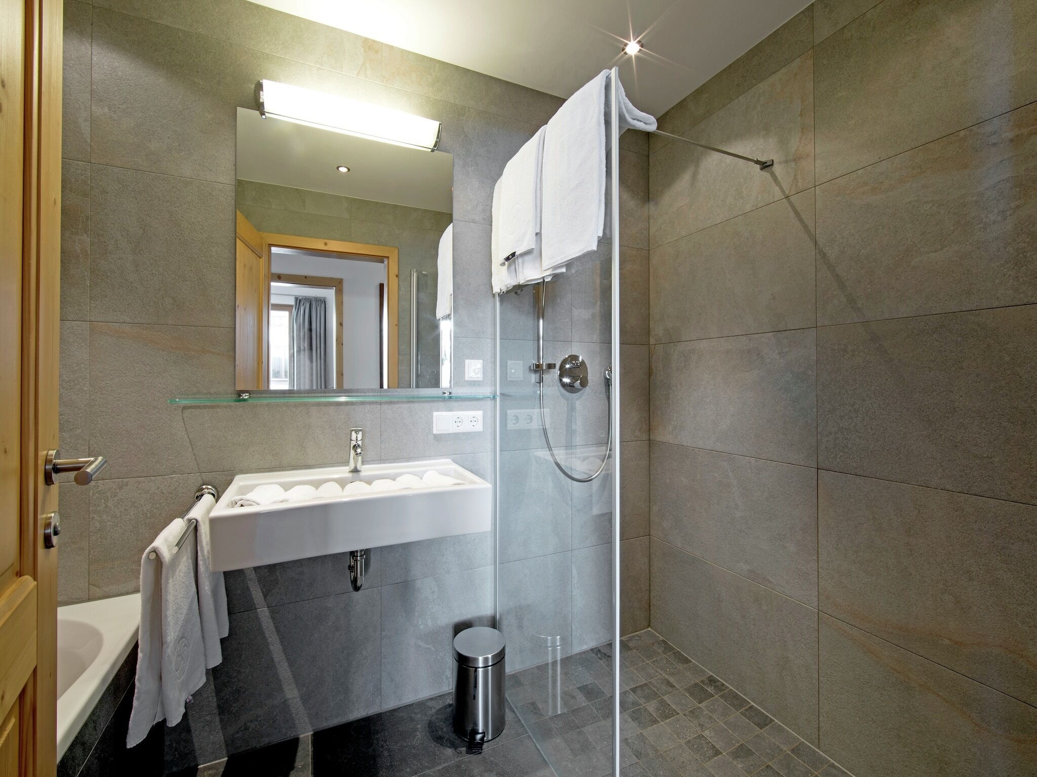 Un baño moderno con cabina de ducha de vidrio, lavabo con espejo e inodoro.