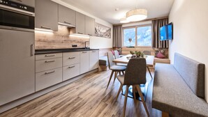 A modern kitchen with a built-in oven, a dining area with a wooden table and chairs, and a large window with a view of a snowy landscape. - Farmhouse in Schwendau near Ski Zillertal (Mayrhofen - Schwendau)