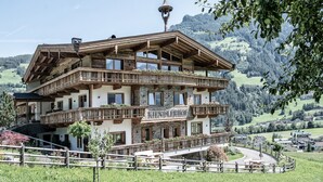 A multi-story chalet with wooden balconies, a stone facade, and a view of a mountainous landscape. - Farmhouse in Schwendau near Ski Zillertal (Mayrhofen - Schwendau)