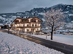 A multi-story wooden building with balconies, surrounded by snow-covered landscape and mountains.