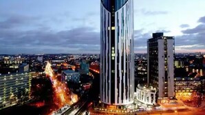 Un grattacielo moderno con un design verticale distintivo, immerso in un panorama urbano al crepuscolo.