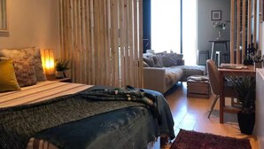 Camera da letto con un letto, comodino, lampada e vista su un'area living con divano e scrivania.