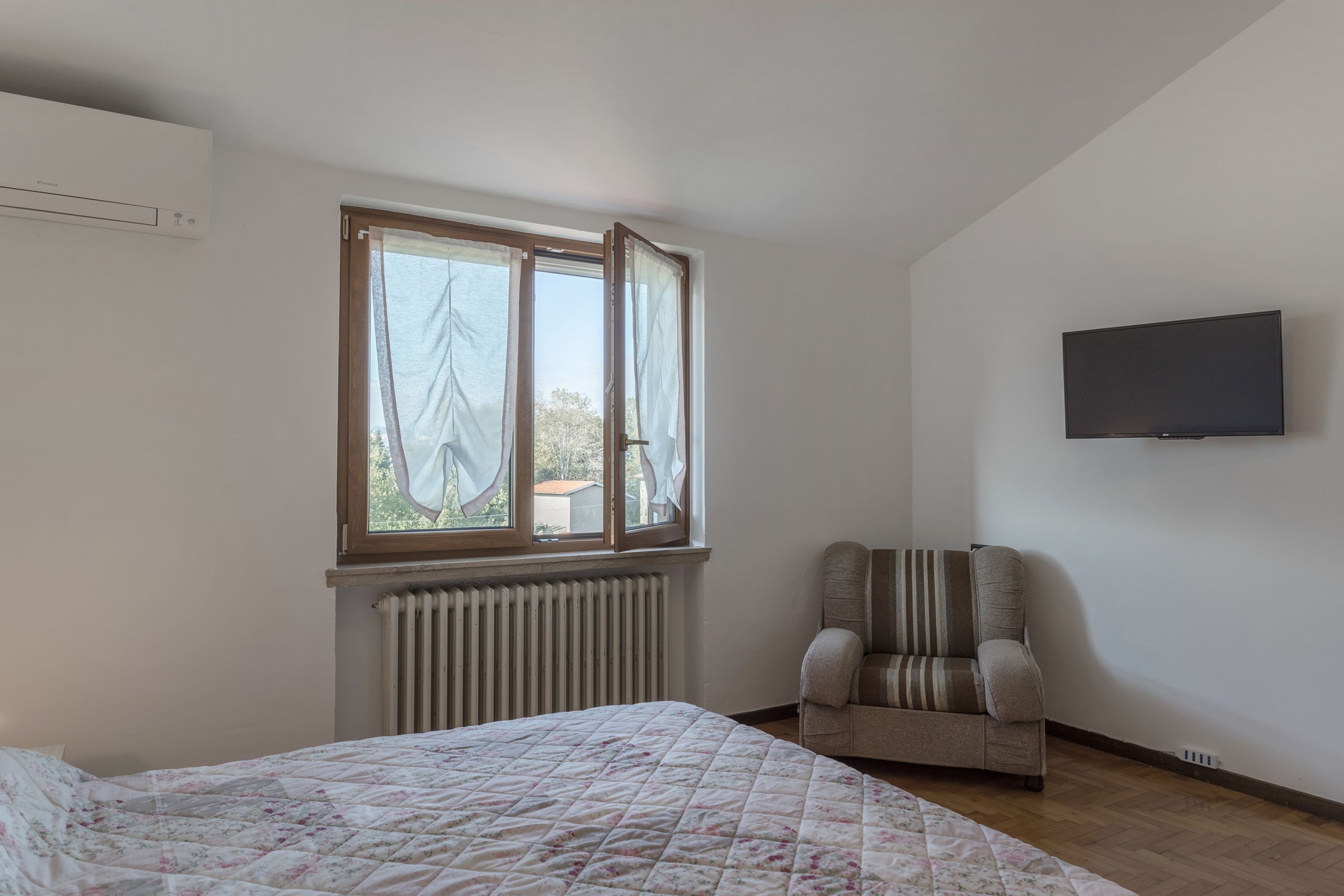 Ein Schlafzimmer mit einem Bett, einem Sessel, einem Fenster und einem Fernseher an der Wand.
