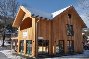 A wooden building with a reception area, large windows, and a snow-covered roof. - Premium apartment with infrared sauna (Kreischberg Murau)