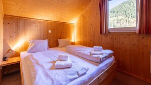 Um quarto de cabana aconchegante com interior de madeira, uma cama com lençóis brancos e uma janela com cortinas.