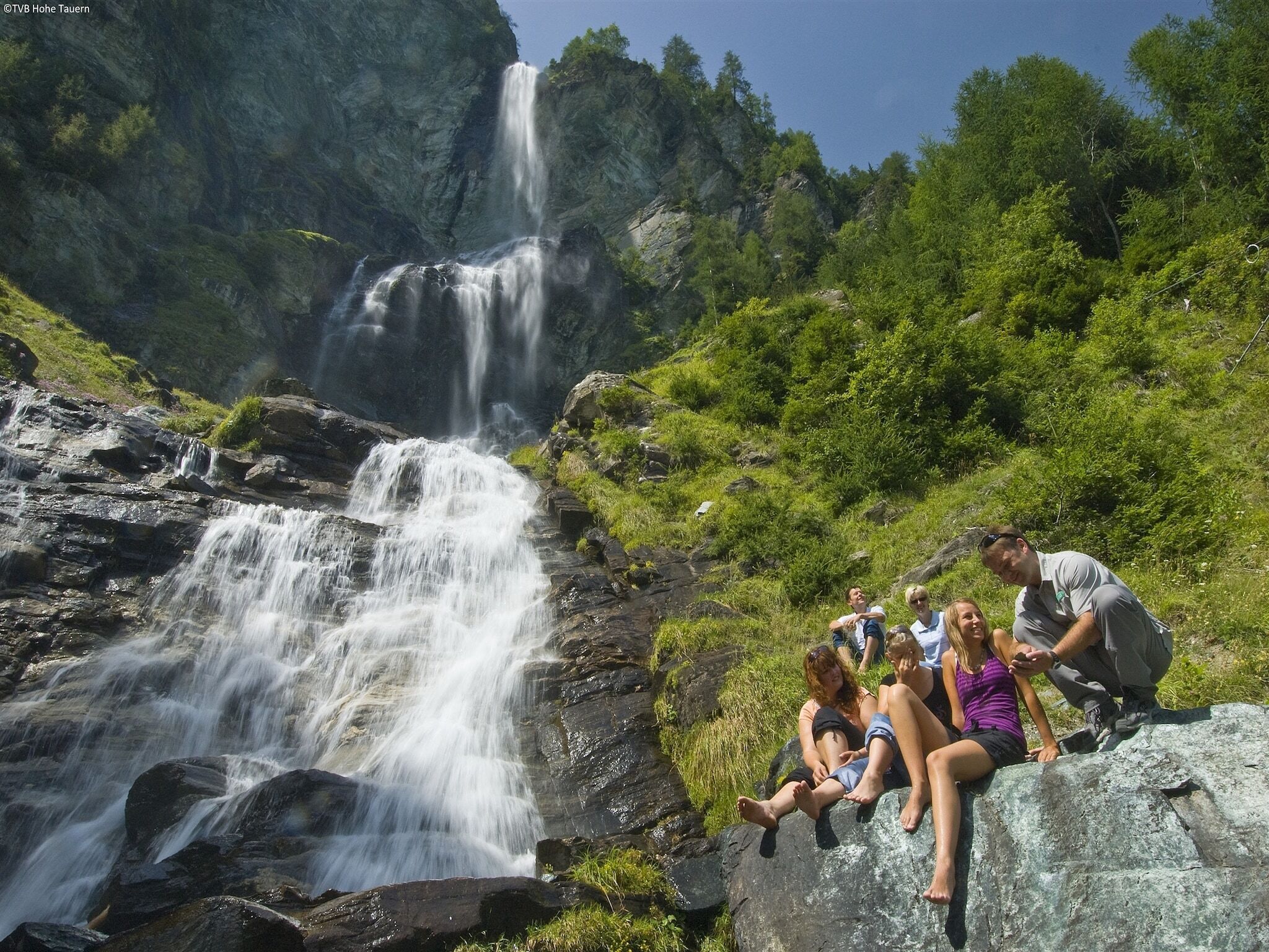 Une cascade d’eau qui dévale des rochers, avec des personnes assises sur une corniche rocheuse.