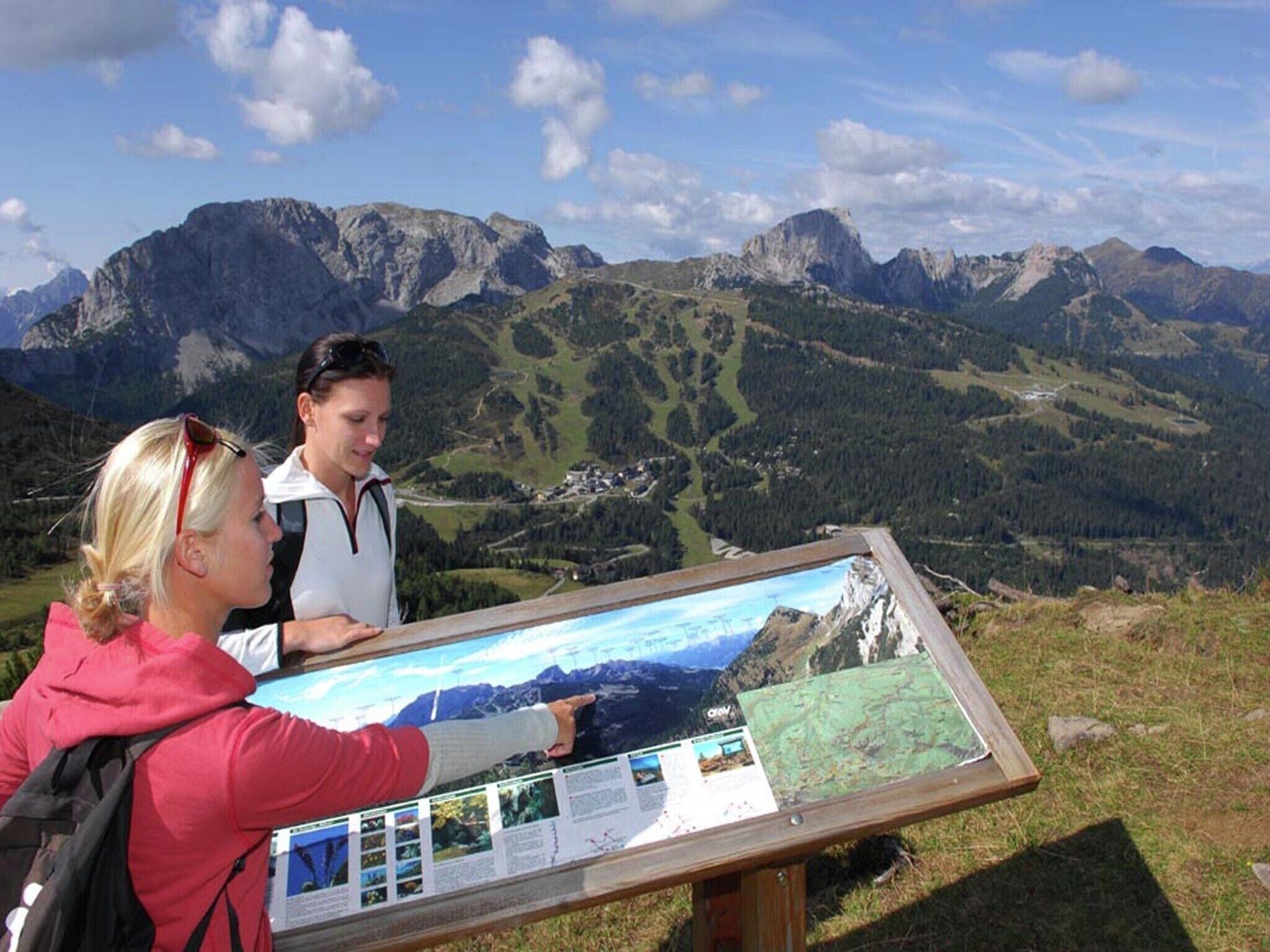 Ein großes Informationsschild mit einer Karte und Text vor einer gebirgigen Landschaft.