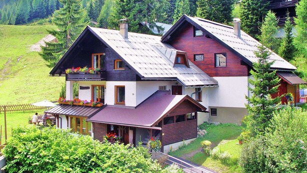A two-story house with a sloped roof, wooden exterior, and a balcony with flower boxes. - Apartment in Nassfeld (Nassfeld)