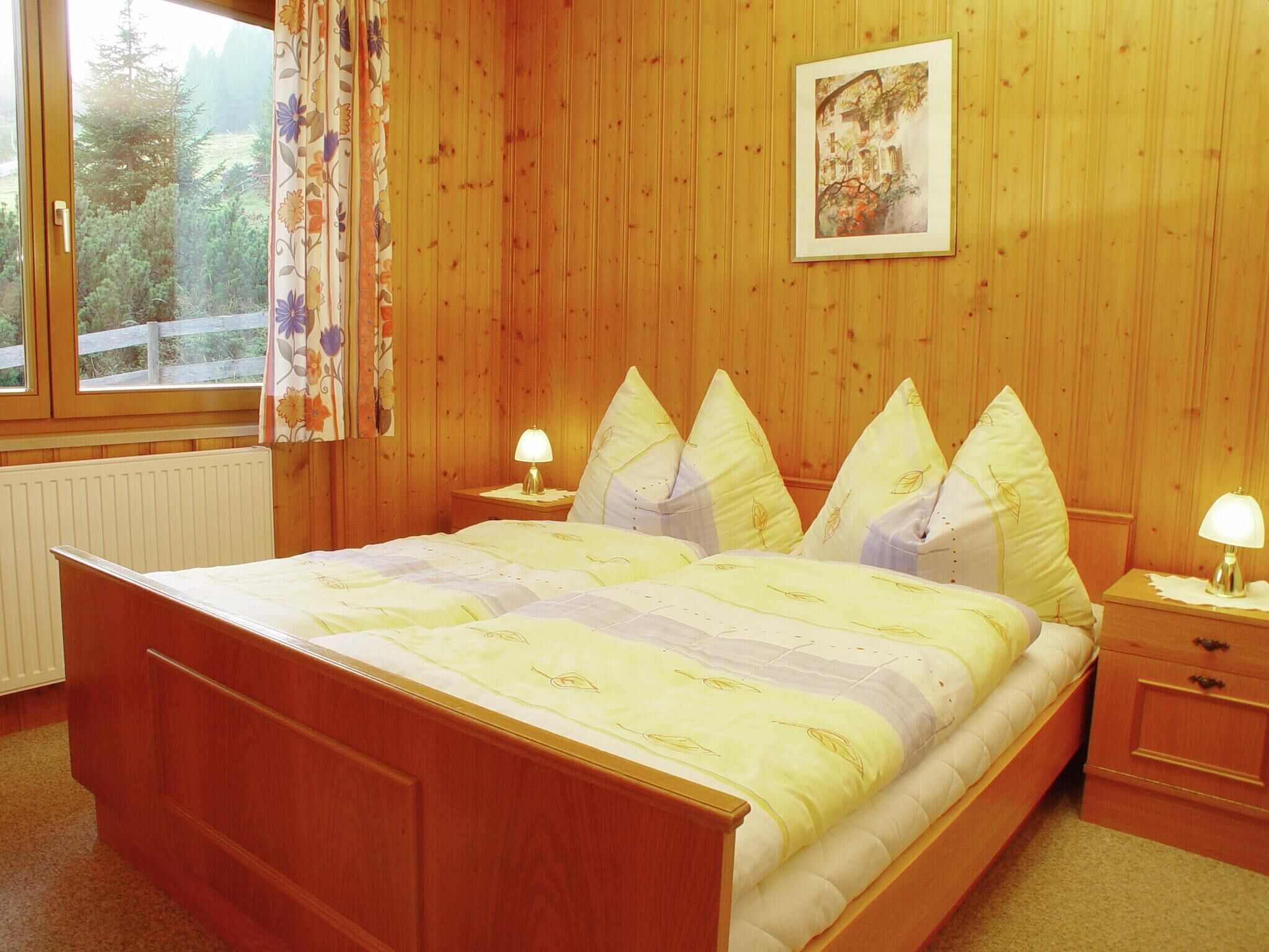 A wooden-paneled bedroom with a bed, two bedside tables, and a window with curtains.