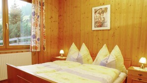 A wooden-paneled bedroom with a bed, two bedside tables, and a window with curtains. - Apartment in Nassfeld (Nassfeld)