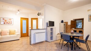 A living room with a sofa, a coffee table, and a TV. There is a dining area with a table and chairs. - La Casa di Daeny in Naples (Naples)