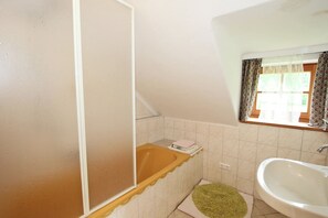 A bathroom with a bathtub, a sink, and a window with curtains.