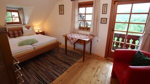 Un dormitorio con cama, una mesita, una silla y ventana con vistas.