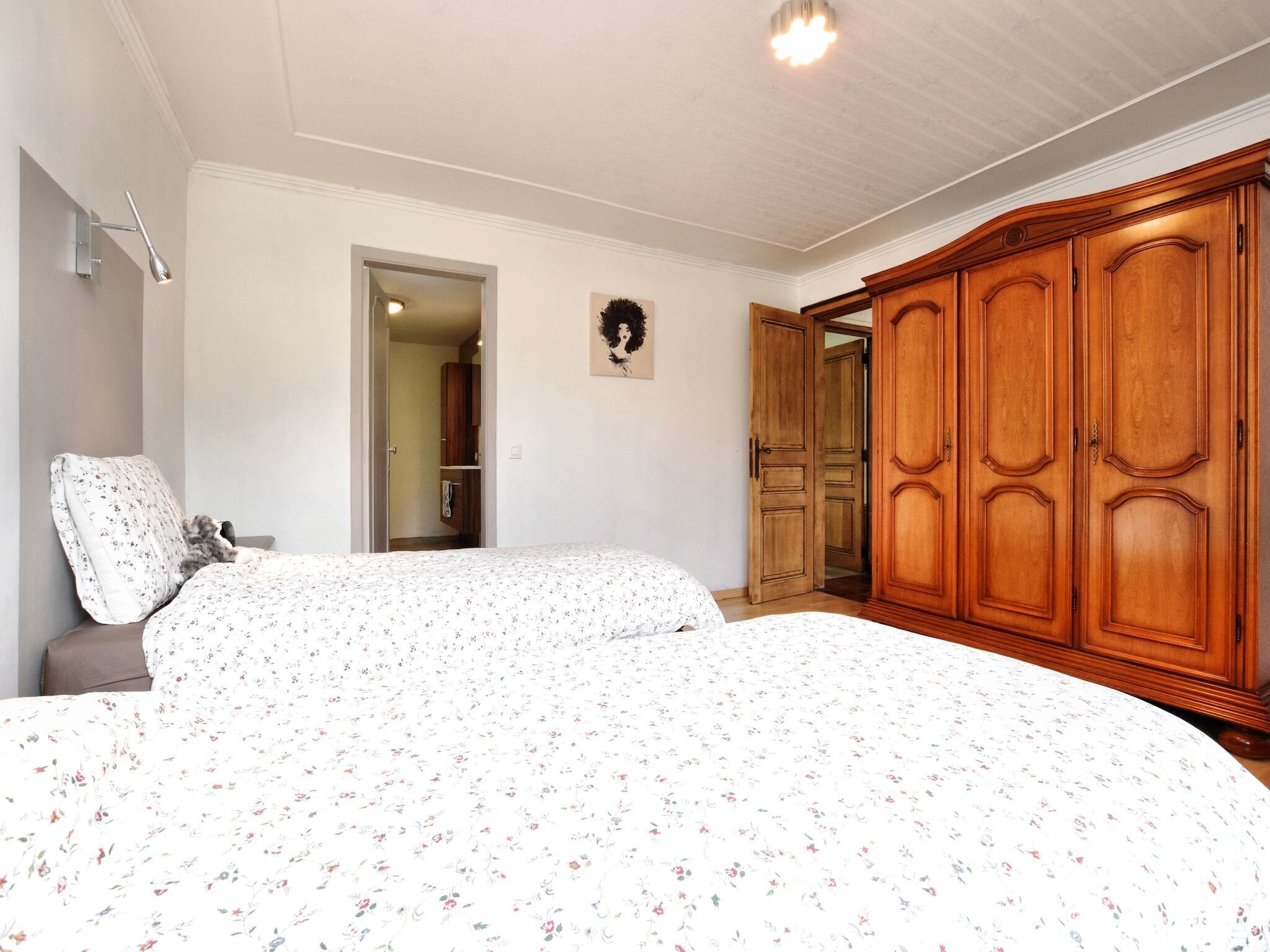 Een slaapkamer met twee bedden, een houten garderobe en een deur naar een andere kamer.