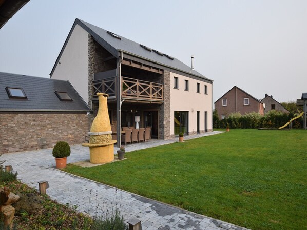 A modern house with a stone facade, a large patio, and a well-maintained lawn.