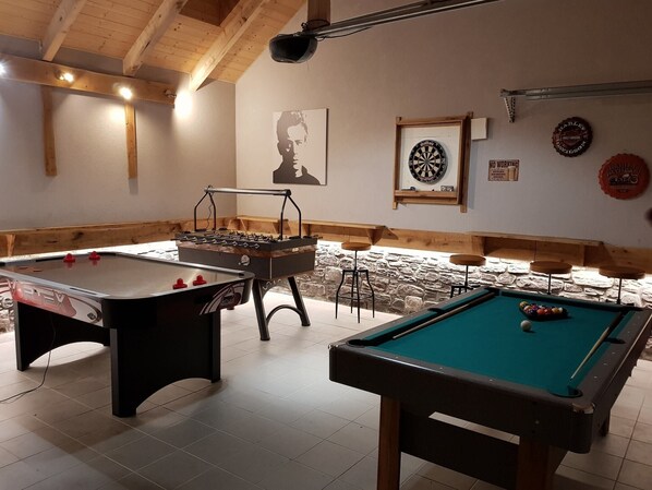 A room with a foosball table, pool table, and dartboard.