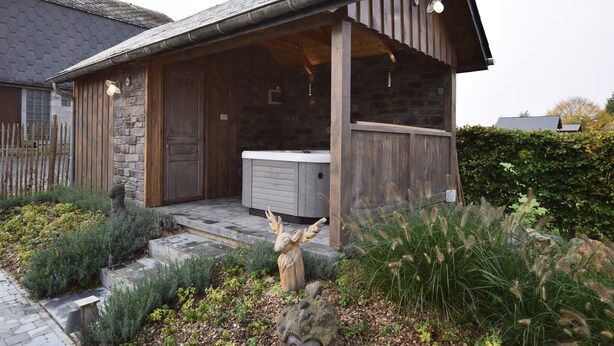 Un chalet rustique avec une façade en pierre, une véranda en bois et un jacuzzi.