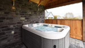 Un bain à remous situé dans un espace extérieur abrité, avec un mur en pierre et des poutres en bois.