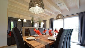 Un espace repas avec une table en bois, des chaises noires et des suspensions en fibres tressées.