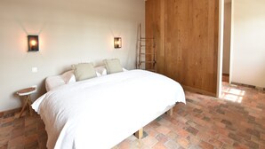 A bedroom with a large bed, two wall-mounted lights, a wooden wardrobe, and a brick floor. - Beautiful Holiday Home with Terrace, Garden (Diksmuide)