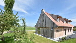 A large, rustic house with a sloped roof and wooden exterior, surrounded by a well-maintained lawn and trees. - Beautiful Holiday Home with Terrace, Garden (Diksmuide)