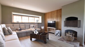 A modern living room with a sectional sofa, a coffee table, a flat-screen TV, and a fireplace. - Beautiful Holiday Home with Terrace, Garden (Diksmuide)