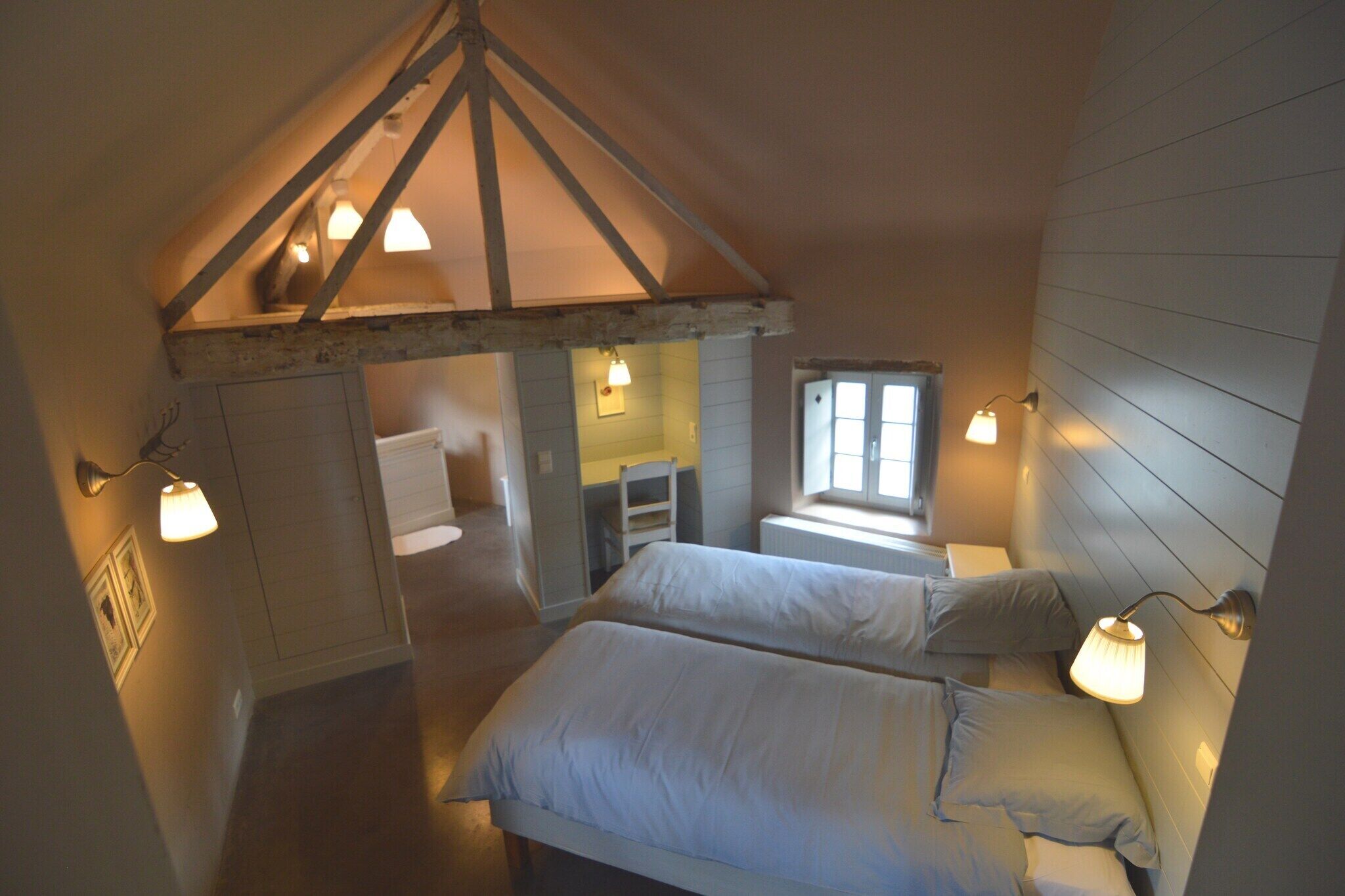 Een gezellige kamer met twee bedden, een houten plafond en een raam dat natuurlijk licht binnenlaat.