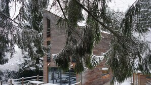 A modern building with a wooden facade and large windows, surrounded by snow-covered trees.