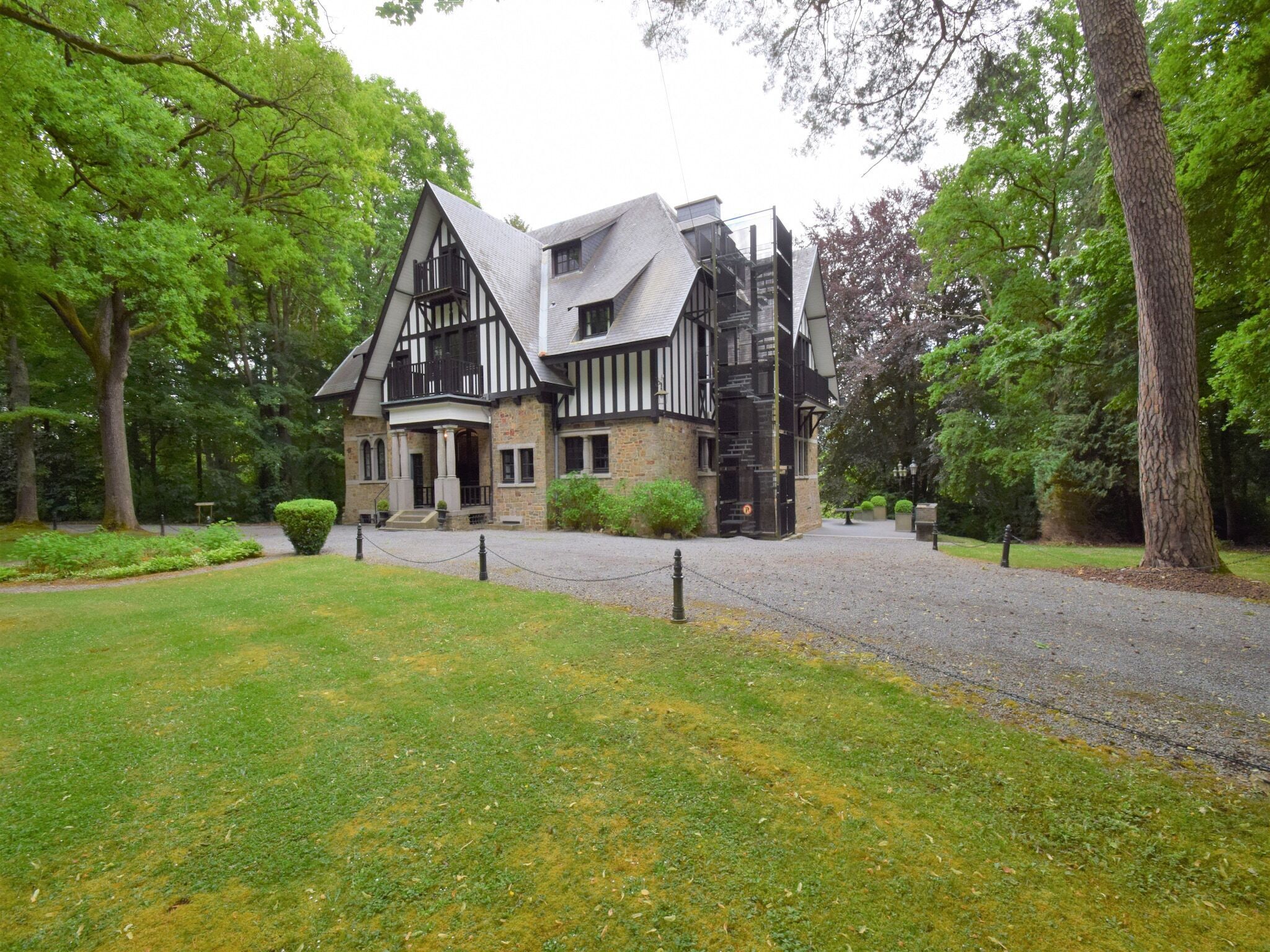 Un bâtiment de style Tudor traditionnel, doté d’une façade symétrique, de toits à pignons très inclinés et d’une entrée centrale surmontée d’un petit porche.