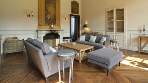 Een ruime woonkamer met een open haard, een groot schilderij en een comfortabele zithoek.