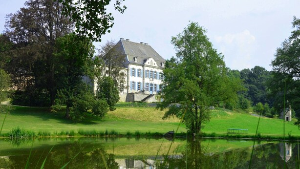 Een groot, historisch gebouw met een symmetrische gevel, een centrale ingang en een spiegelbeeld in stil water.