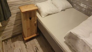 Un dormitorio pequeño con una mesita de noche de madera, una cama individual con ropa de cama blanca y una ventana con persianas.