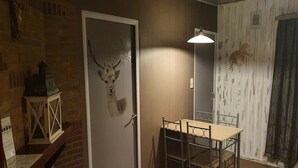 Un comedor con una mesa y sillas, una puerta decorada con una cabeza de ciervo y un farol en una pared de ladrillo.