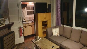 Una sala de estar con sofá, mesa de centro, chimenea y una cocina visible a través de una puerta abierta.