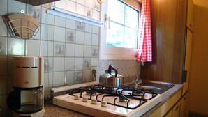 Una cocina con estufa a gas, cafetera y ventana con cortina a cuadros.