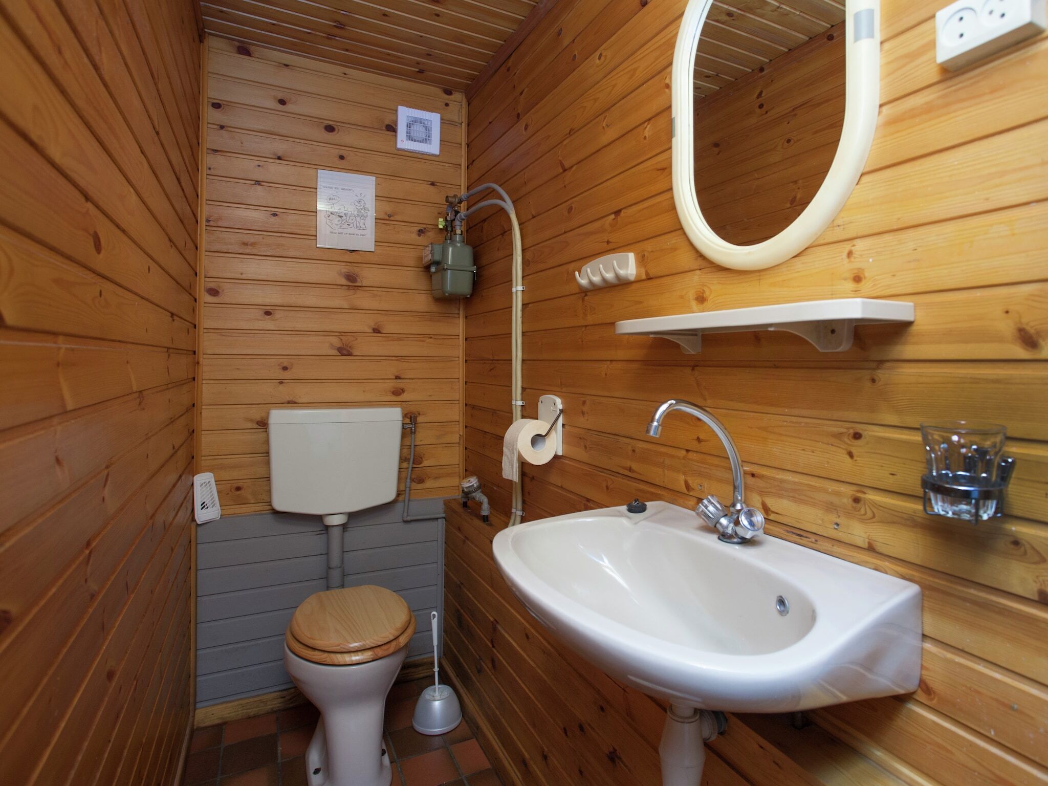 A wooden-paneled bathroom with a toilet, sink, and mirror.