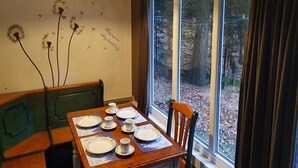 A dining area with a table set for four, a bench, and a window with a view of a wooded area.